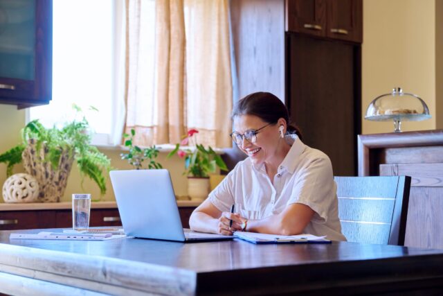 Woman sitting at kitchen table smiling at laptop