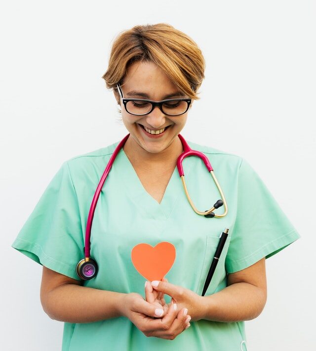 Nurse smiling and looking down at a paper heart she's holding