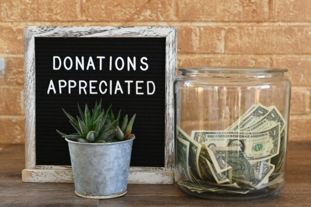 Glass jar of dollar bills next to a house plant and a donation sign